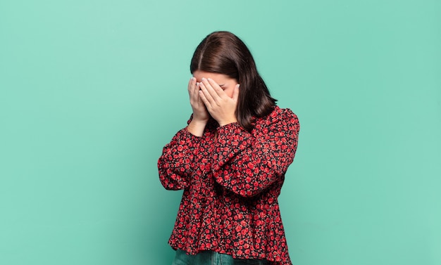 Giovane donna abbastanza casual che copre gli occhi con le mani con uno sguardo triste e frustrato di disperazione, pianto, vista laterale