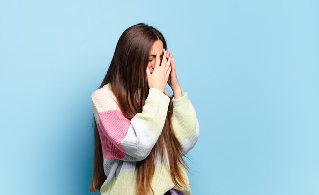 Giovane donna abbastanza casual che copre gli occhi con le mani con uno sguardo triste e frustrato di disperazione, pianto, vista laterale