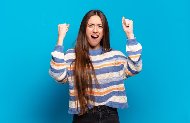 Giovane donna abbastanza casual che grida in modo aggressivo con un'espressione arrabbiata o con i pugni chiusi per celebrare il successo