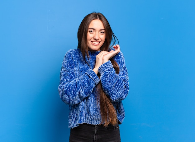 Giovane donna abbastanza casual che si sente innamorata e sembra carina, adorabile e felice, sorridendo romanticamente con le mani accanto al viso