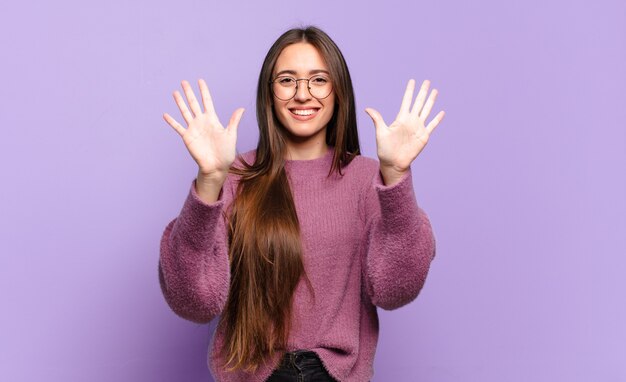 Giovane donna abbastanza casual che sorride e sembra amichevole, mostrando il numero dieci o decimo con la mano in avanti, conto alla rovescia