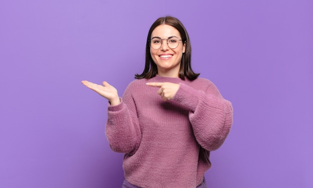 Giovane donna abbastanza casuale che sorride allegramente e che indica lo spazio della copia