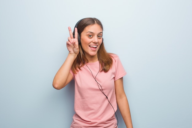 Giovane donna abbastanza caucasica divertente e felice facendo un gesto di vittoria. Sta ascoltando musica con le cuffie.