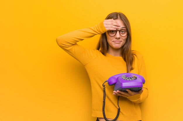 Giovane donna abbastanza caucasica preoccupata e sopraffatta. Ha in mano un telefono vintage.