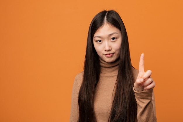 Giovane donna abbastanza cinese che mostra numero uno con il dito.