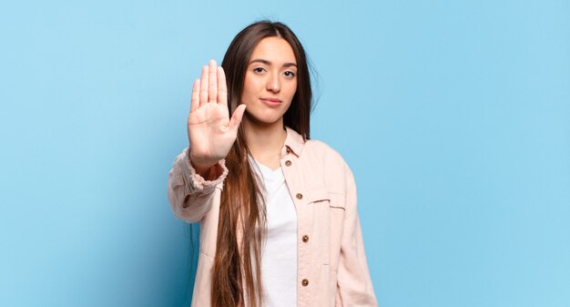 Giovane donna abbastanza informale che sembra seria, severa, dispiaciuta e arrabbiata che mostra il palmo aperto che fa il gesto di arresto