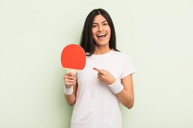 Giovane donna abbastanza ispanica che sembra eccitata e sorpresa che indica il concetto di ping pong laterale