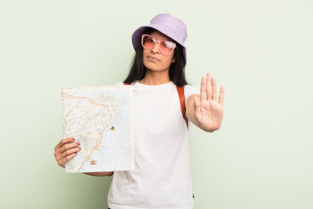 Giovane donna abbastanza ispanica che sembra seria mostrando il palmo aperto facendo il gesto di arresto turistico e il concetto di mappa