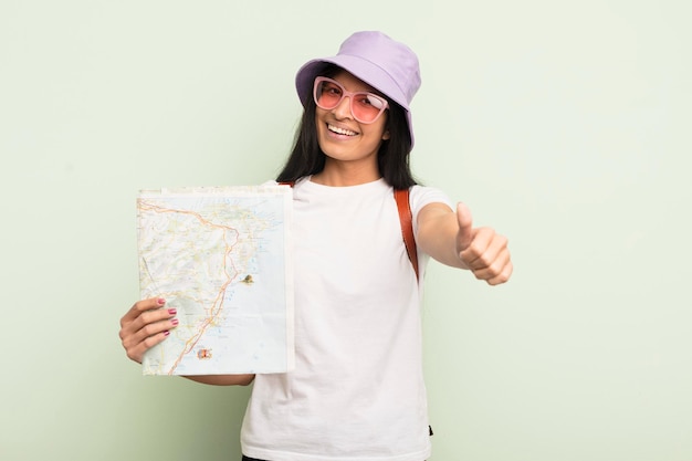 Giovane donna abbastanza ispanica che si sente orgogliosa di sorridere positivamente con i pollici in su turistico e concetto di mappa