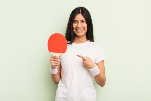 Giovane donna abbastanza ispanica che sorride allegramente, sentendosi felice e indicando di lato. concetto di ping pong