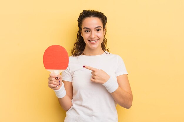 Giovane donna abbastanza ispanica che sorride allegramente sentendosi felice e indicando il concetto di ping pong laterale