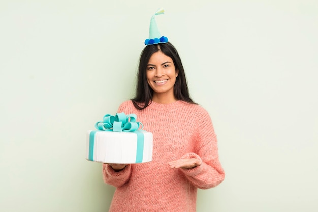 Giovane donna abbastanza ispanica che sorride allegramente sentendosi felice e mostrando un concetto di torta di compleanno di concetto