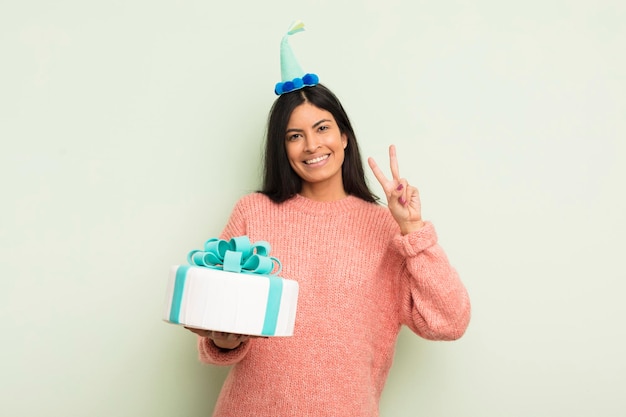 Giovane donna abbastanza ispanica che sorride e che sembra felice gesturing vittoria o concetto di torta di compleanno di pace