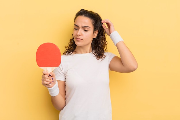 Giovane donna abbastanza ispanica che sorride felicemente e sogna ad occhi aperti o dubita del concetto di ping pong