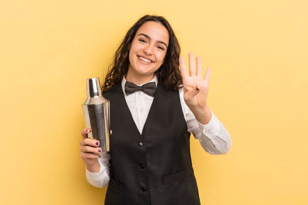 Giovane donna abbastanza ispanica sorridente e dall'aspetto amichevole che mostra il barista numero quattro e il concetto di cocktail