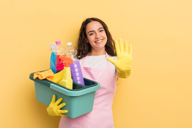 Giovane donna abbastanza ispanica sorridente e dall'aspetto amichevole che mostra il numero cinque lavori domestici un concetto di prodotti puliti