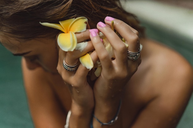 giovane donna abbronzata in piscina in fiori di frangipani