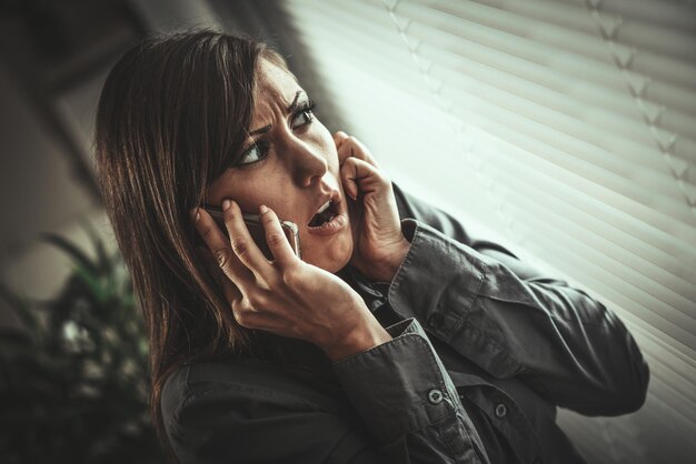 Giovane donna abusata spaventata guardando attraverso la finestra in cerca di sicurezza.