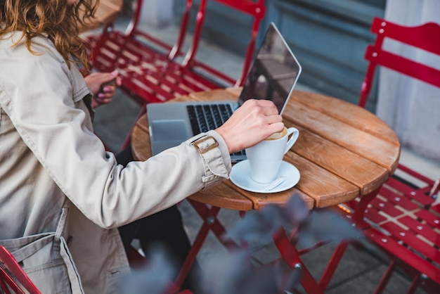 Giovane donna adulta che lavora al computer portatile in un caffè all'aperto con una tazza di latte