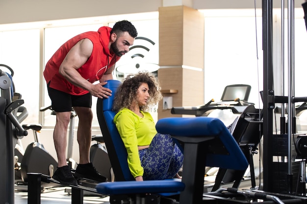 Giovane donna adulta che lavora in palestra facendo esercizi per le gambe sulla macchina con l'aiuto del suo personal trainer