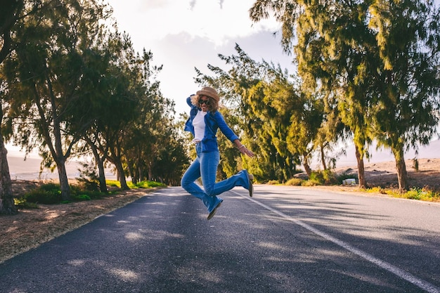 Giovane donna adulta che salta felice nel mezzo di una lunga strada asfaltata diritta Concetto di persone di viaggio e libertà emozioni di felicità Le donne casuali si divertono e si godono le vacanze di viaggio su strada