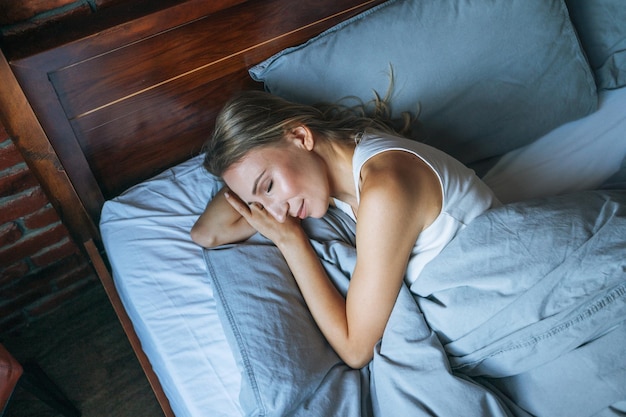 Giovane donna adulta con capelli lunghi biondi che dorme sul letto nella stanza del soppalco a casa