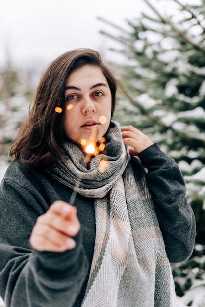 Giovane donna adulta con stelle filanti sulla pineta invernale