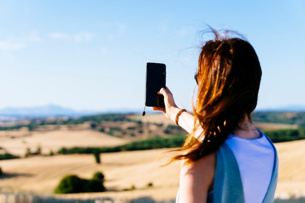 Giovane donna adulta di spalle che scatta una foto del tramonto con lo smartphone