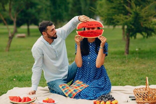 Giovane donna adulta e uomo coppia picnic al prato di erba verde nel parco divertendosi con l'anguria