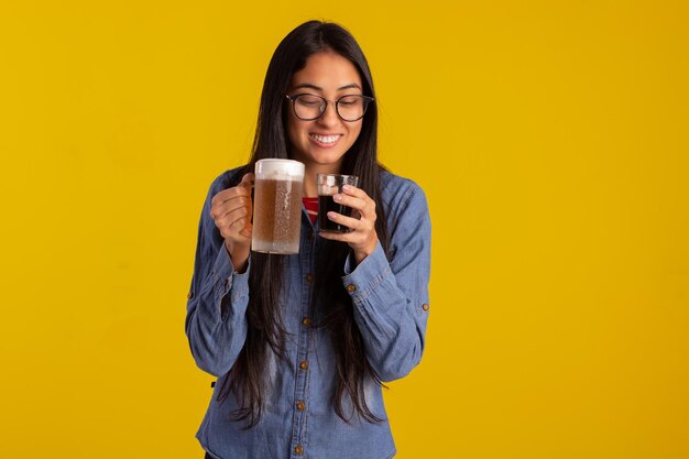 Giovane donna adulta in foto in studio che fa espressioni facciali e tiene in mano un bicchiere di birra e una tazza di caffè