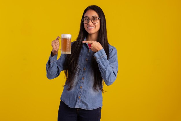 Giovane donna adulta in foto in studio che fa espressioni facciali e tiene un bicchiere di birra