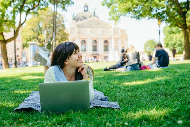 Giovane donna adulta posa con il computer portatile nel parco cittadino sull'erba verde