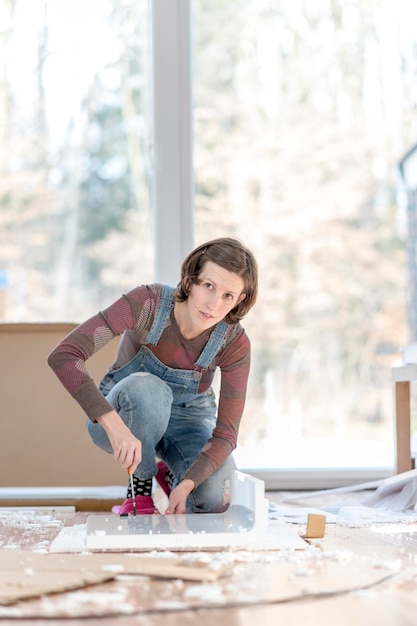 Giovane donna adulta single in tuta che lavora sul pavimento con vecchi mobili o progetti in casa