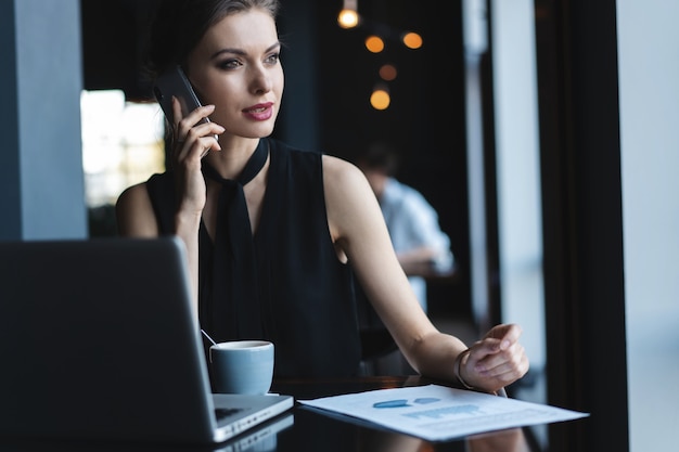 Giovane donna affascinante che chiama con il cellulare mentre è seduta al bar durante il tempo libero, una donna attraente che parla con il cellulare mentre riposa al bar.