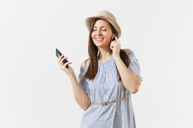 Giovane donna affascinante in abito, cappello che ascolta musica in auricolari sul telefono cellulare, divertiti, rilassati isolato su sfondo bianco. Persone, emozioni sincere, concetto di stile di vita. Zona pubblicità. Copia spazio.