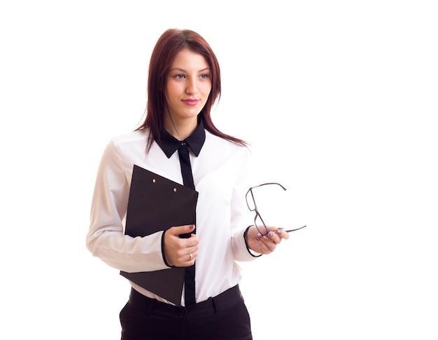 Giovane donna affascinante in camicia bianca e pantaloni neri con lunghi capelli scuri che tiene i suoi occhiali neri e una cartella su sfondo bianco in studio