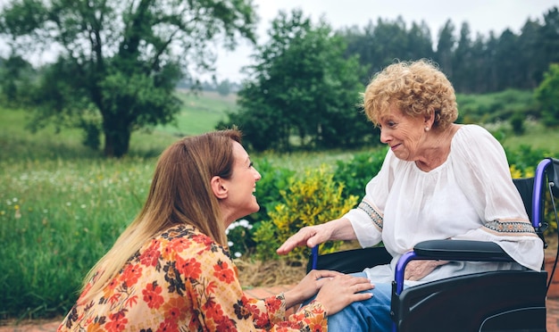 Giovane donna affettuosa che parla con una donna anziana su una sedia a rotelle in giardino