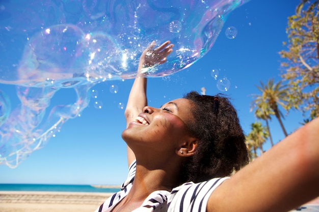 Giovane donna africana che gioca con le bolle di sapone all&#39;aperto alla spiaggia