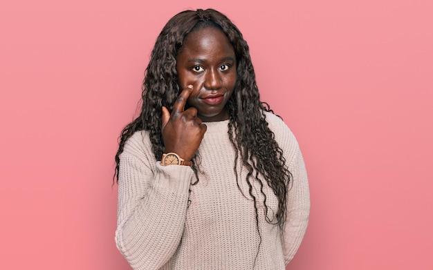 Giovane donna africana che indossa un maglione invernale di lana che punta all'occhio che ti guarda gesto, espressione sospetta