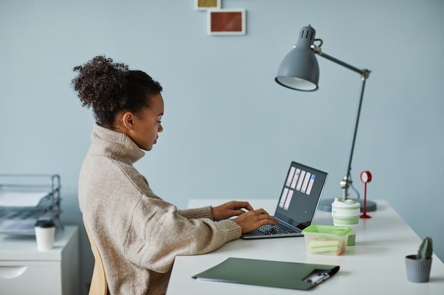 Giovane donna africana che lavora con un progetto online sul computer portatile seduto al suo posto di lavoro in ufficio