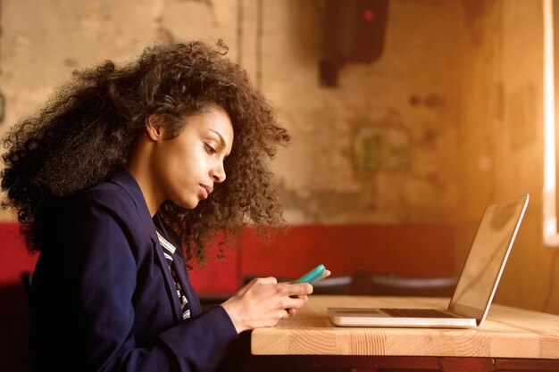 Giovane donna africana che si siede in un caffè utilizzando il telefono cellulare