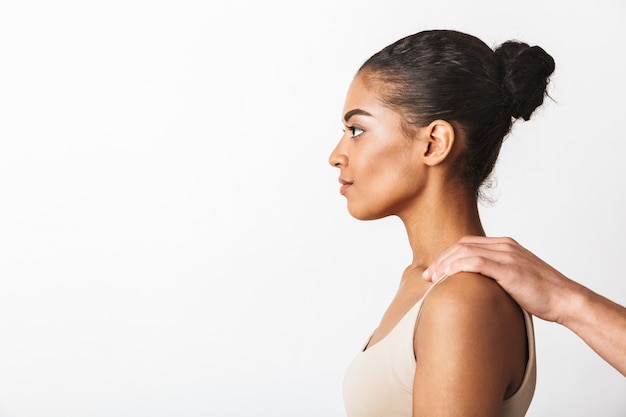 Giovane donna africana che si siede mentre la mano dell'uomo che tiene le sue spalle isolate su bianco