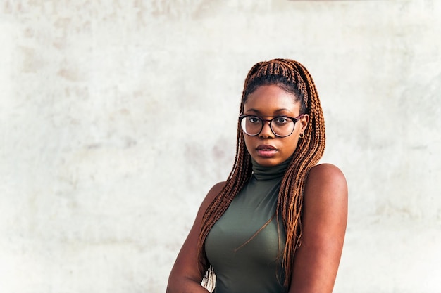 Giovane donna africana con gli occhiali che guarda la fotocamera con muro di cemento grigio sullo sfondo, concetto di gioventù e diversità razziale, copia spazio per il testo