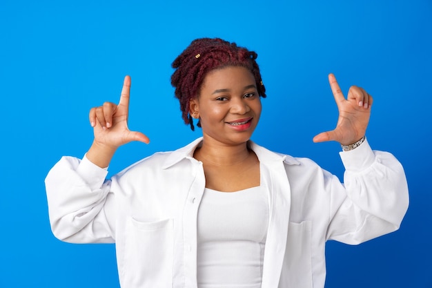 Giovane donna africana sorridente che fa cornice con le mani contro la superficie blu