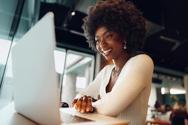 Giovane donna africana sorridente che si siede con il computer portatile in caffè