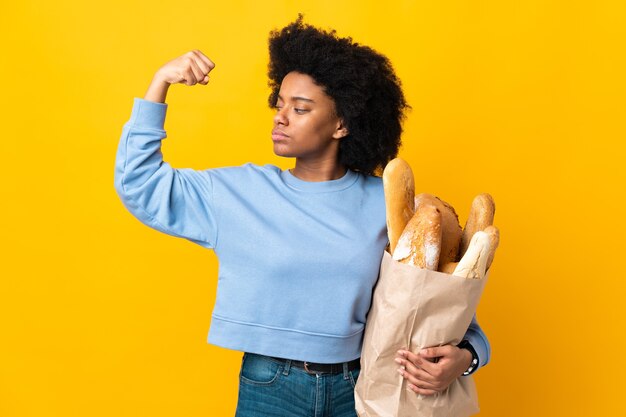 Giovane donna afro-americana che compra qualcosa di pane isolato su giallo facendo un forte gesto