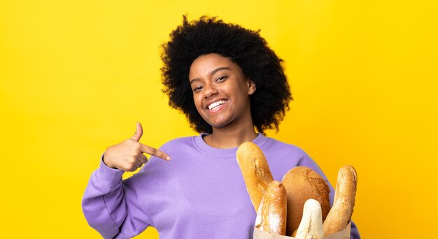Giovane donna afro-americana che compra qualcosa di pane isolato su giallo orgoglioso e soddisfatto di sé