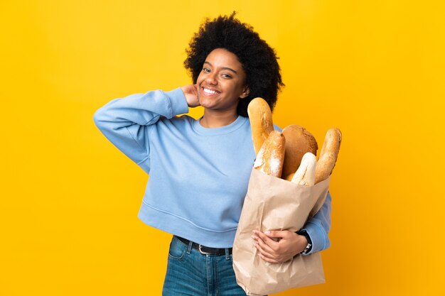 Giovane donna afro-americana che compra qualcosa di pane isolato su giallo ridendo