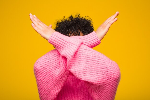 Giovane donna afro-americana che indossa un maglione rosa mantenendo due braccia incrociate, rifiuto.