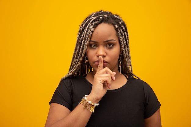 Giovane donna afro-americana che segnala silenzio. Ragazza con il dito in bocca per chiedere silenzio.